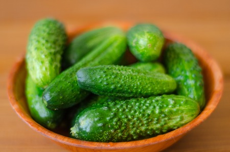 green fresh cucumbers in a wooden bowl on a wooden tableの写真素材