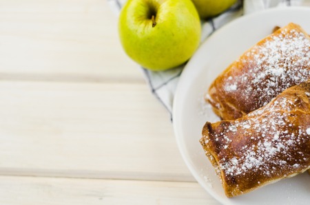 Freshly baked apple pie on plate and two fresh yellow apples on light wooden background and towelの写真素材