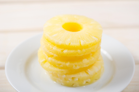 Pieces of pineapple. Pineapple chopped into round pieces in a pile on a white plate on a white wooden backgroundの写真素材