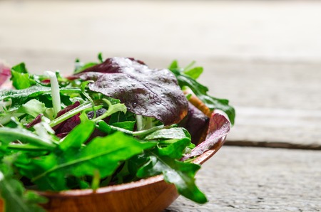 Fresh green salad. Mix of leaves of arugula, lettuce in a wooden bowl on a wooden table. Vegetarian dish.の写真素材