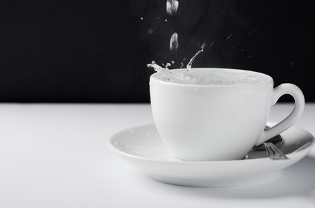 White mug for tea on a white table with pouring hot water.の写真素材