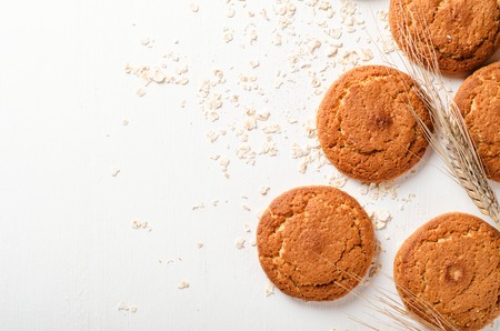 Oatmeal cookies with oat flakes and spikelets on a white wooden background. Copy space, top view.の写真素材