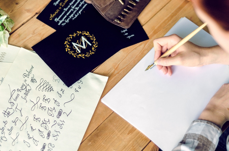 A girl calligrapher paints pen on white paper behind her working wooden table.の写真素材