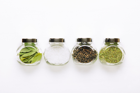 Popular spices in small jars on a white background. Bay leaf, sea salt, pepper and herbs. Top viewの写真素材