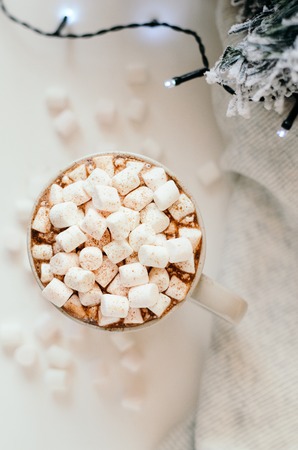 Hot cocoa with marshmallow, cinnamon, warm cozy light plaid, Christmas tree branches and a garland on white table. Top view.の写真素材