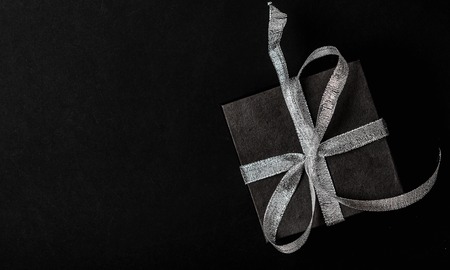 Black gift box with silver ribbon bow on black background. Top view, copy spaceの写真素材