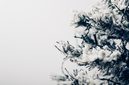 Artificial fir-tree with snow on a white background with an electric garland. Toned photo.の写真素材