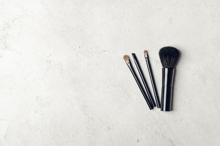 Black makeup brushes on a light stone background. Professional tools for make-up artist. Flat Lay,...