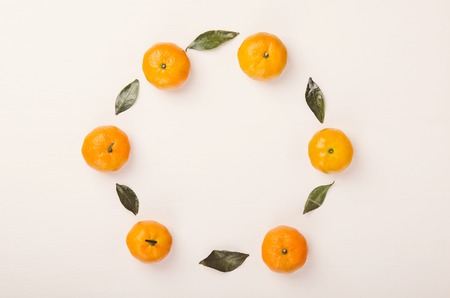Round frame of small tangerines and green leaves on white background. Healthy fruits, food. Copy space, top view, flat layの写真素材
