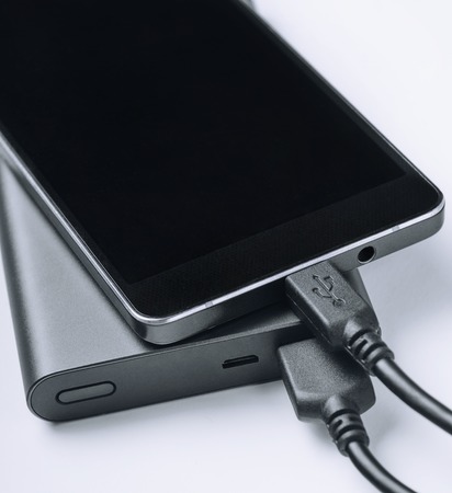 Black phone smartphone charging from power bank on white background. Modern technology concept.
