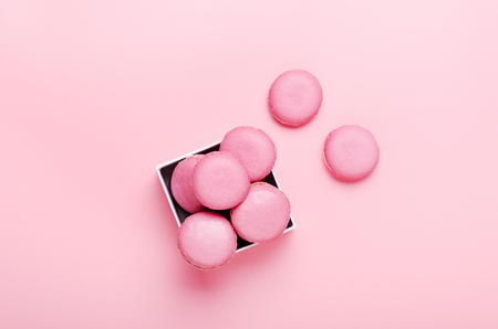 Pink macaroon cookies on a pink background in box. The concept of sweets, pastries, junk food. Minimal composition. Top view, flat layの写真素材
