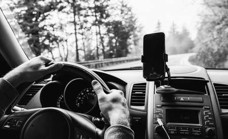 A man is driving on a mountain road and we see his hands, interior car console and smartphone.の写真素材