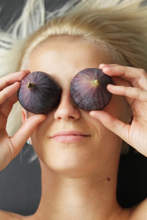 Young woman holding figs fruit in her hand near face
