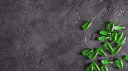 Transparent green matte gel capsules of herbal marijuana oil on a gray concrete background. The...