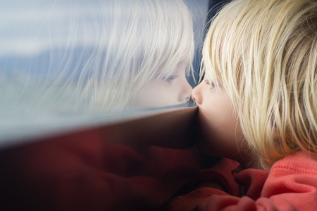 Cute young child deep in thought looking out of a window