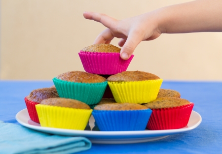 Plate of colourful home-made muffins for a children's party, with a child's hand is reaching for a muffin.の写真素材