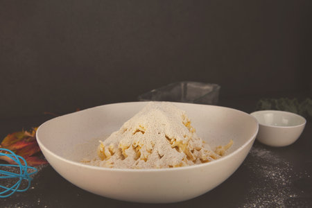 Grated butter mixed into flour with eggs, oil and autumn leaves around - cozy homemade baking preparation in a rustic fall kitchen.の写真素材