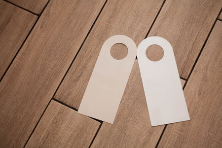 Two blank door hanger mockups in white on a wooden surface. Ideal for hotel branding, âDo Not Disturbâ or cleaning service signage design templates.の写真素材