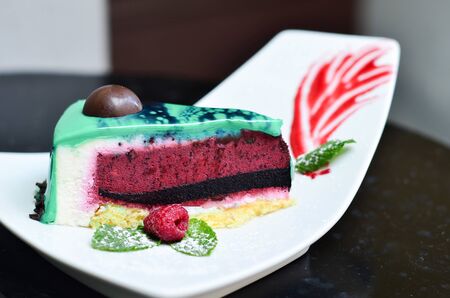 sweet cake with colored cakes and icing with berries and mint on a plate