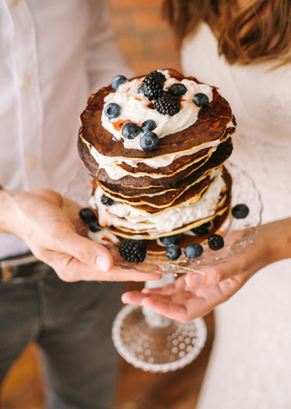 The groom and the bride hold in hand cake from pancakes. Cake from pancakes with whipped cream and...