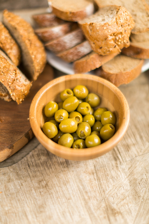 the cut whole-grain bread and green olives on a wooden backgroundの写真素材