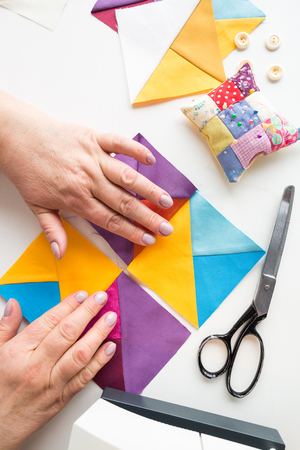 female hands coordinates geometric color fabric pieces for patchwork quilt on a white background. the process of creating scrappy blankets. top view. flat lay.の写真素材