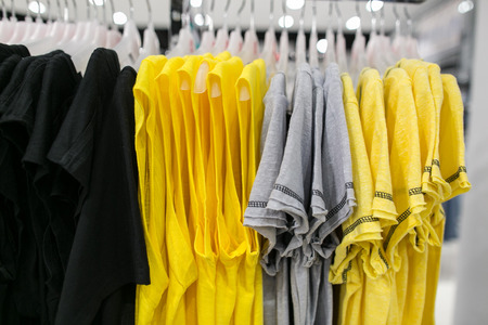 Tshirts on hangers in shop. Clothes in yellow tones. Gray tshirts. Clothes in black tones.の写真素材