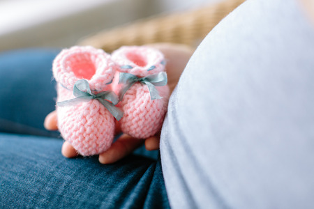 future mother knows a sex of her baby. pregnancy concept. Pregnant woman holding pink knitted baby bootees at a stomach with selective focus.の写真素材
