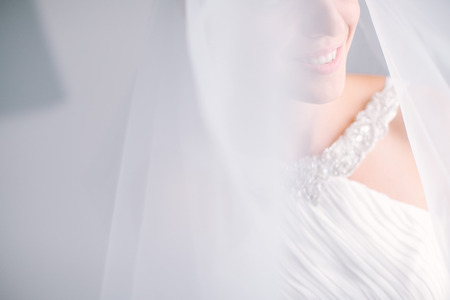 smile of the beautiful bride in a white dress under a veil close up. blurred photo, empty space for the text. wedding concept. Fine art wedding.の写真素材