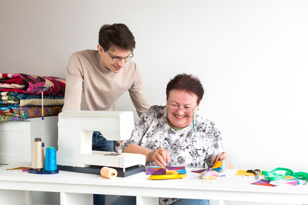 patchwork and quilting tailor - two smiling tailors at work in the studio bent over multi-colored patchwork cloth lying on the table near the sewing machine. Sewing concept. Startup, Family business.の写真素材