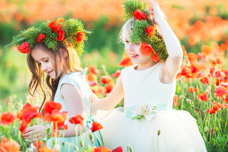 little girl model, poppies, summer fashion concept - close-up on girly games in the field of poppies, two girlfriends hugging. happy, smiling cute princeses with a wreath of fresh poppy.の写真素材