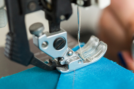 needlework and quilting in the workshop of a tailor - close-up on the needle of the sewing machine stitches the pieces of colored blue fabricの写真素材