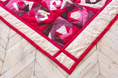 Part of color patchwork quilt with purple flowers pattern as background. Pink Scrappy blanket....