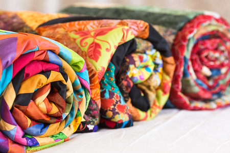 Three colored patchwork quilts twisted into close up. Colorful scrappy blankets folded as background. Handmade, hobby, art concept.の写真素材