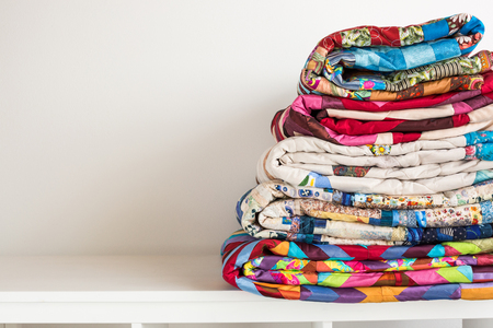 sewing and fashion concept - stack of colorful quilts, beautiful bedspreads stacked in several rows...