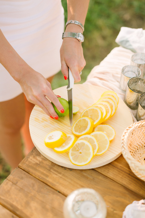 food, health, lifestyle, vegetarianism, cooking, nature concept - womans hands with bright orange manicure, silver bracelet and wrist watch slice lemon and lime on white plateの写真素材