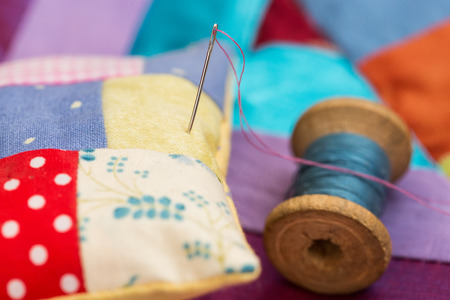 patchwork, quilting, sewing, tailoring and fashion concept - close-up beautiful colorful stitched cushion and needle, macro on pillow with background of blue, lilac and red flaps of fabricの写真素材