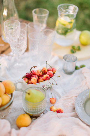 picnic, lifestyle, vegetarianism, celebration, wedding concept - still-life with tableware: plates, crystal globes, gravy boat full of cherries and jug of lemonadeの写真素材