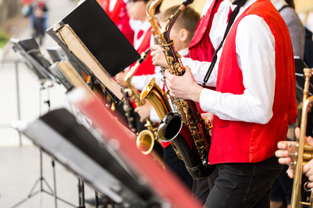 Musical instrument, brass band and orchestra concept - festive performance of saxophones, closeup on sax and sheet music stands, musicians in red concert jackets and shirts, selective focusの写真素材