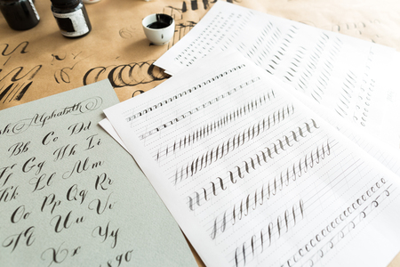 calligraphy, education, graphic design concept. lots of exercises for training skills of calligraphy with help of special supplies like black ink, brushes and white lined sheetsの写真素材