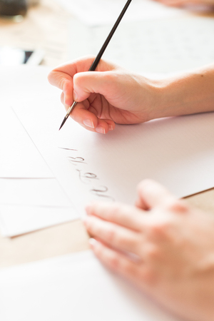 penmanship, hobby, graphic design concept. well groomed hands of young caucasian woman who writing letters of russian alphabeth in harmonious and aesthetic manner with ink and brushの写真素材