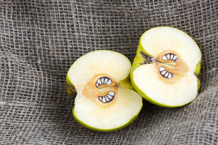 fall, imagination, natural product. close up of two halves of healthy fruit called quince placed on the very textured grey burlap. its pits looked like teeth and it seems that fruit is agressiveの写真素材