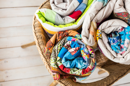 patchwork and fashion concept - closeup on three beautiful quilts rolled into a tube and laid in a wicker chair, warehousing of finished products on a white background, top view, flat layの写真素材