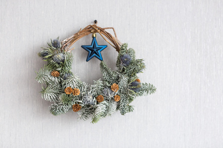 interior design, new year, religion concept. on the light grey background of the wall there is christmas wreath, that is hanging on the nail, amazingly decorated with burdocks and tiny pineconesの写真素材