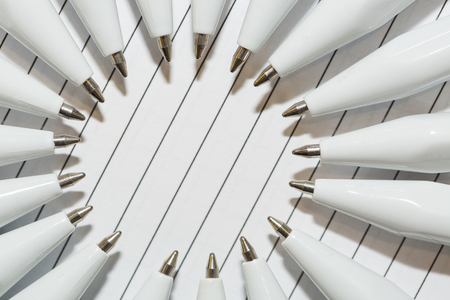 polygraphy, office work, equipment concept. close up of silver tips of white ballpoint pen that are arranging and they form a round on the background of white ruled paperの写真素材