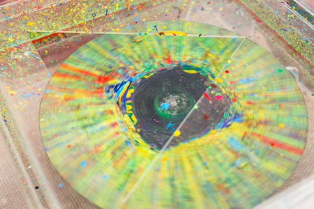 Electric machine placed in plastic box with hole in form of triangle with circle inside of it that is covered by multicolored paints and spinning around itselfの写真素材