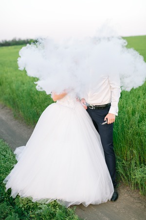 love, smoking, wedding concept. there is a newly married couple of lovers dressed for ceremony of engagement, she is in white dress and he is in official costume, they have their heads in the cloudsの写真素材