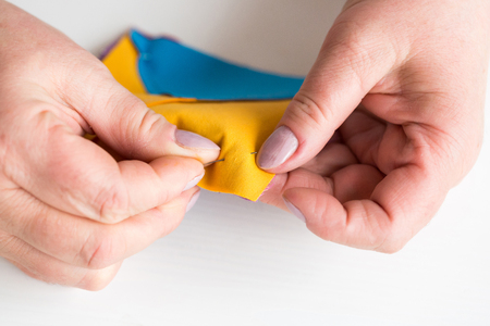 hobby, quilting, industry concept. clowe up of soft delicate hans of old female dressmaker, she is holding few pieces of fabric in yellow and blue colouresの写真素材