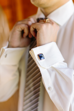 wedding, elegance, high fashion concept. close-up arms of the groom in a white shirt with blue cufflinks, straightening tieの写真素材