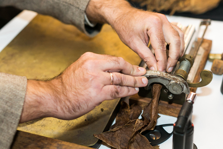 The man making cigars from tobacco leaves using a mechanical device and press.の写真素材